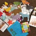 A collection of children's items on a brown carpet, including animal figures, a puzzle with children and animals, two small books, laminated cards, and colorful plastic animals like a duck and a starfish.