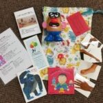 A sensory activity kit on a textured brown carpet includes a colorful drawstring bag, a Mr. Potato Head toy, cards with images and instructions, a book, and laminated photo cards of feet and hands.