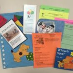 A literacy activity kit featuring a blue bag with a dog design, a "Where's Spot?" book, activity sheets, a DVD, pamphlets, and two small toy dogs. The items are arranged on a flat surface.